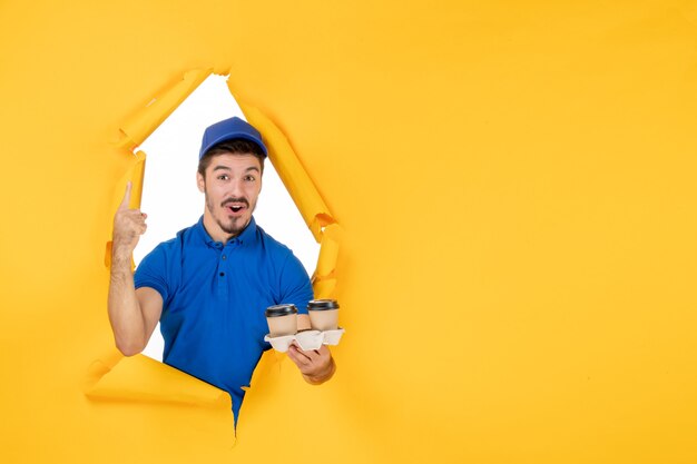 Vorderansicht männlicher Kurier in blauer Uniform mit Kaffeetassen auf gelbem Raum