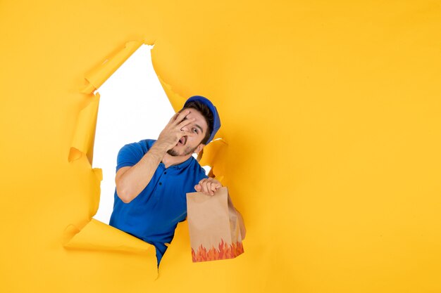 Vorderansicht männlicher Kurier in blauer Uniform mit Lebensmittelpaket auf gelbem Raum