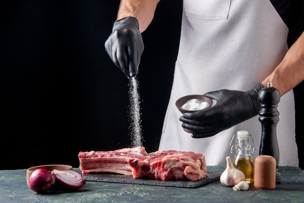 Kostenloses Foto vorderansicht männlicher metzger, der fleisch auf dunkler oberfläche salzt