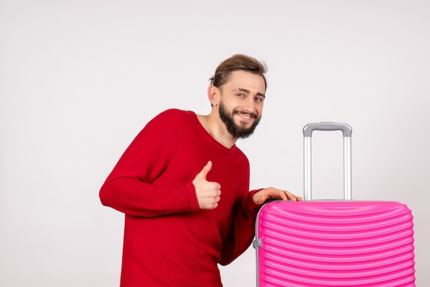 Vorderansicht männlicher Tourist mit rosa Tasche lächelnd auf weißer Wand