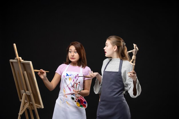 Vorderansicht Malerinnen, die menschliche Figur auf Staffelei auf schwarzer Wand zeichnen Fotofarbe zeichnen Gemälde Job-Kunst-Künstler-Bild