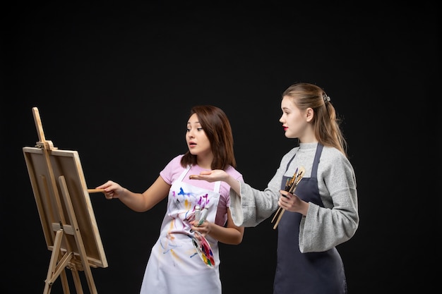 Kostenloses Foto vorderansicht malerinnen zeichnen auf staffelei auf der schwarzen wand farbe zeichnen malerei job kunst foto künstler bild