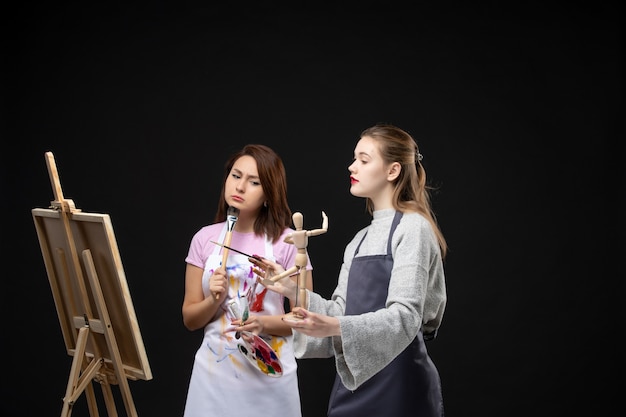 Vorderansicht Malerinnen zeichnen auf Staffelei auf schwarzen Wandfarben zeichnen Malerei Job Kunst Foto Künstler Bild