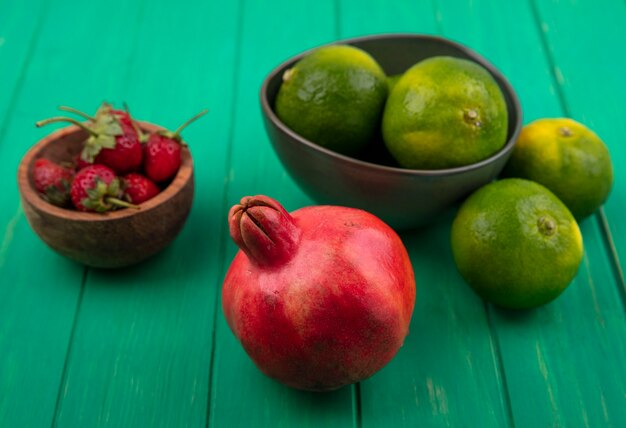 Vorderansicht Mandarinen in einer Schüssel und Granatapfel mit Erdbeeren auf einer grünen Wand