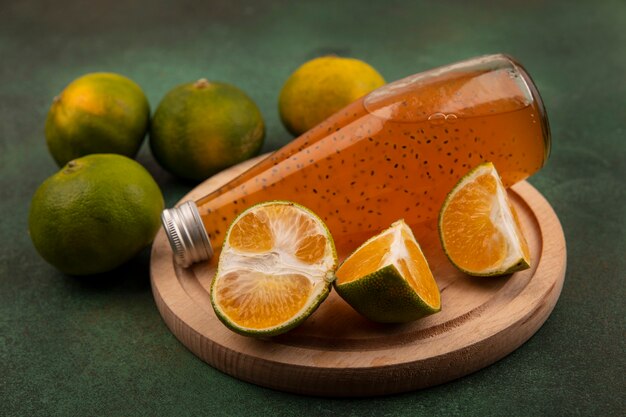 Vorderansicht Mandarinenscheiben mit einer Flasche Saft auf einem Ständer an einer grünen Wand