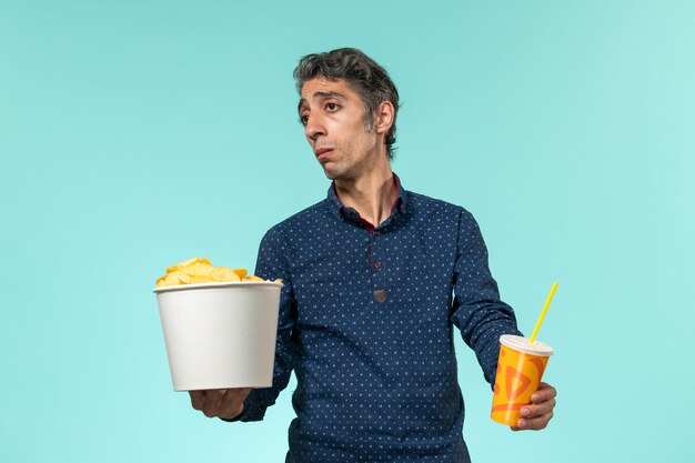 Vorderansicht Mann mittleren Alters, der Kartoffelspitzen und Soda auf einem blauen Schreibtisch hält