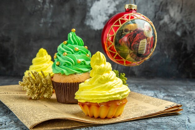 Vorderansicht Mini bunte Cupcakes roter Weihnachtsbaum Spielzeug auf Zeitung auf dunklem Hintergrund Neujahrsfoto