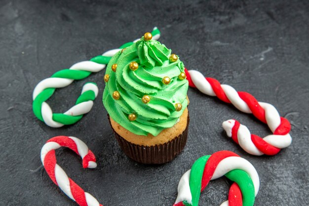 Kostenloses Foto vorderansicht mini-weihnachtsbaum-cupcake und weihnachtssüßigkeiten auf dunklem hintergrund