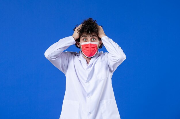 Vorderansicht nervöser männlicher Arzt in medizinischem Anzug mit roter Maske auf blauem Hintergrund Drogenvirus Covid-Impfstoff Gesundheitsmedizin Krankenhaus pandemische Farben