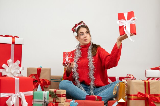 Vorderansicht neugieriges Mädchen mit Weihnachtsmütze, die Geschenke hält, die um Geschenke sitzen