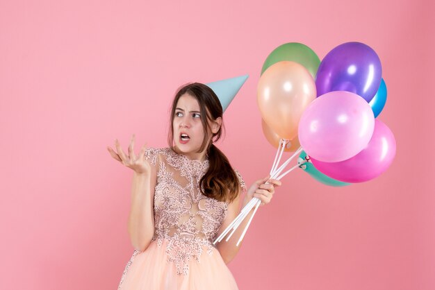 Vorderansicht niedliches Partygirl mit Partykappe, die Ballons etwas hält