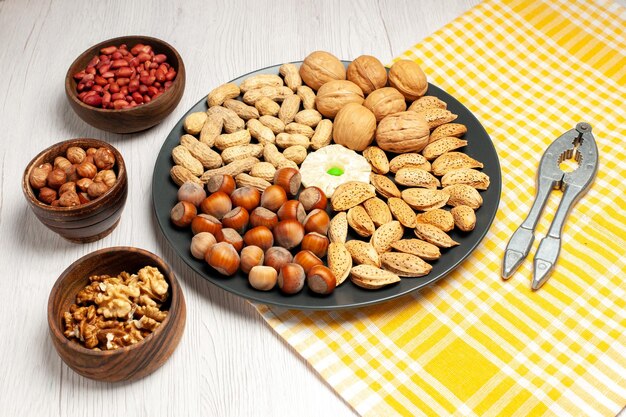 Vorderansicht Nüsse Zusammensetzung frische Walnüsse Erdnüsse und Haselnüsse innerhalb der Platte auf weißem Schreibtisch Nuss viele Baum Snack Pflanzenschale