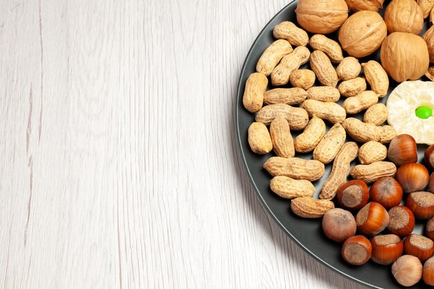 Vorderansicht Nüsse Zusammensetzung frische Walnüsse Erdnüsse und Haselnüsse innerhalb der Platte auf weißem Schreibtisch Nussbaum Snack Pflanze viele Schale