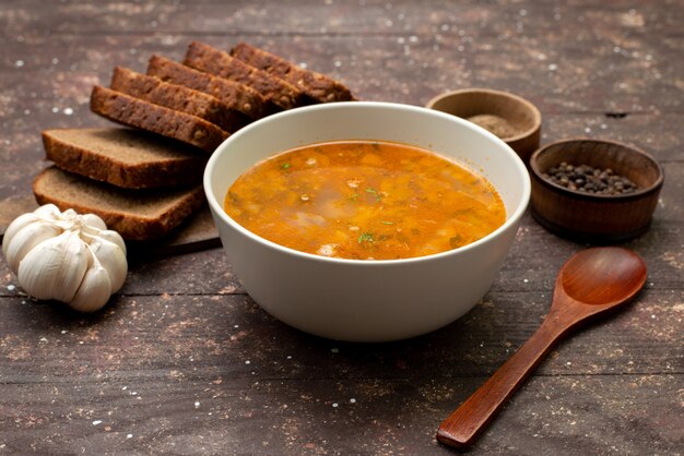 Vorderansicht orange Gemüsesuppe mit Brotlaib und Knoblauch auf braunem, Essen Mahlzeit Suppe Brot
