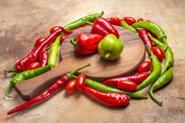 Vorderansicht Paprika auf einem Schneidebrett, umgeben von Paprika und Kirschtomaten auf bernsteinfarbenem Hintergrund