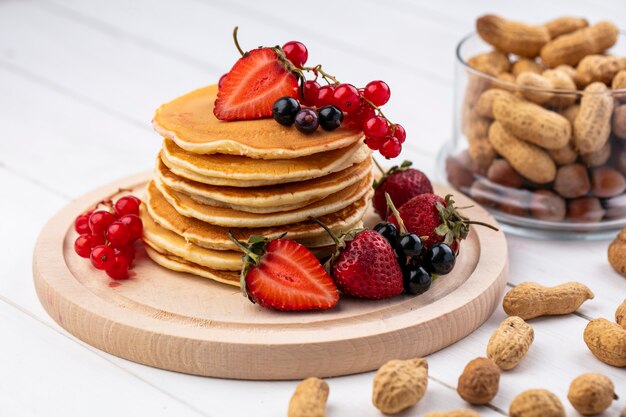 Vorderansicht Pfannkuchen mit Erdbeeren schwarzen und roten Johannisbeeren auf einem Tablett mit Erdnüssen