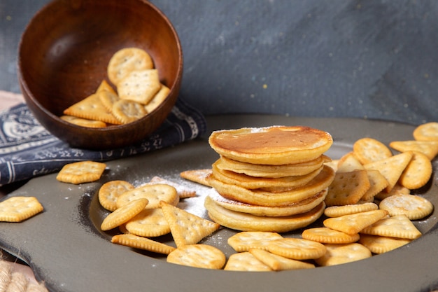 Vorderansicht Pfannkuchen und Cracker innerhalb Platte auf grau