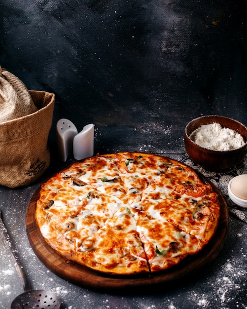 Vorderansicht Pizza mit roten Tomaten und Käse auf dem braunen hölzernen runden Schreibtisch und grauem Boden