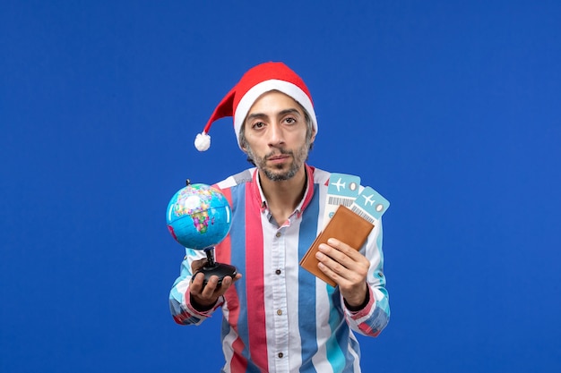 Vorderansicht regulärer Mann mit Tickets und Globus auf Neujahrsfeiertag der blauen Wand Emotionen
