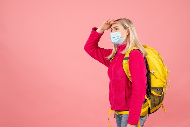 Vorderansicht reisende Frau mit gelbem Rucksack, der Maske trägt, die Hand auf ihre Stirn setzt