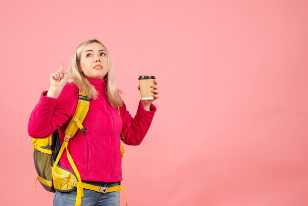 Vorderansicht reisende Frau mit Rucksack, der Finger oben hält Kaffeetasse zeigt