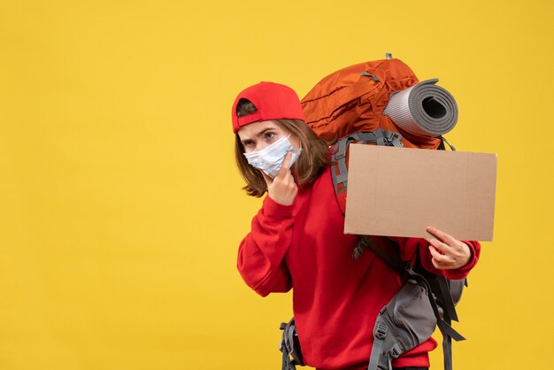 Vorderansicht reisendes Mädchen mit Rucksack und Maske, die Pappe hält