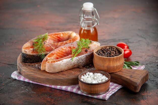 Vorderansicht rohe Fischscheiben mit Tomaten und Gewürzen auf dunklem Fleischgericht Foto