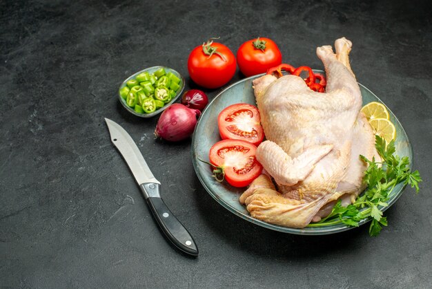 Vorderansicht rohes frisches Huhn innerhalb der Platte mit Grüns und Gemüse auf dunklem Hintergrund Fleischfutter Huhn Tier