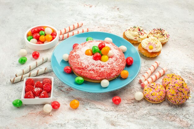 Vorderansicht rosa Kuchen mit bunten Bonbons auf weißem Hintergrund Goodie Regenbogen Süßigkeiten Dessert Farbkuchen