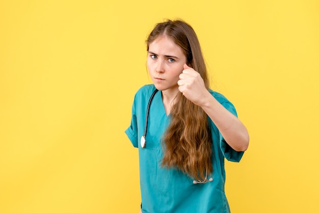 Vorderansicht Ärztin, die auf gelbem Hintergrundmedizinerkrankenhausgesundheitsemotion droht