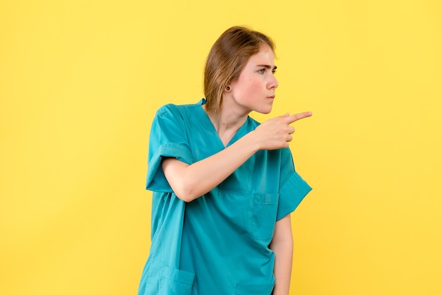 Vorderansicht Ärztin, die auf gelbes Hintergrundgesundheitsmediziner-Emotionskrankenhaus zeigt