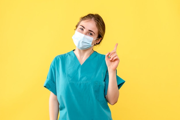 Vorderansicht Ärztin, die in Maske auf gelbem Hintergrundgesundheitskrankenhauspandemie-Covid lächelt