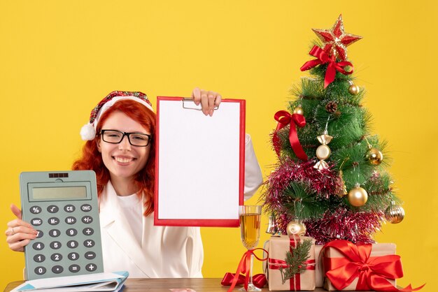 Vorderansicht Ärztin, die Rechner um Weihnachtsgeschenke und Baum hält