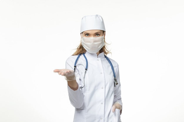 Vorderansicht Ärztin im medizinischen Anzug mit Maske und Handschuhen aufgrund von Coronavirus auf weißer Schreibtisch-Covid-Pandemie-Virus-Krankheit