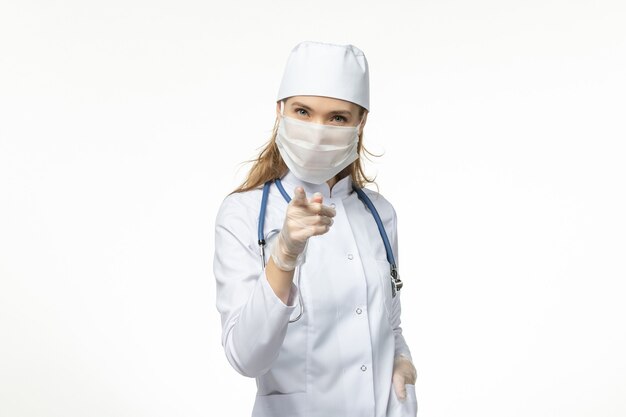 Vorderansicht Ärztin im medizinischen Anzug mit Maske und Handschuhen aufgrund von Coronavirus auf weißer Wand Covid-Pandemic Disease Virus-Krankheit