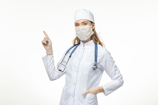 Vorderansicht Ärztin im medizinischen Anzug mit Maske und Handschuhen aufgrund von Coronavirus auf White Desk Disease Pandemie Covid-Virus