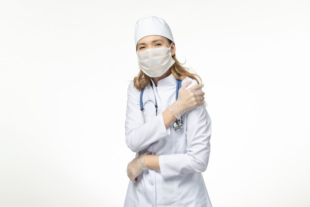 Vorderansicht Ärztin im medizinischen Anzug mit Maske und Handschuhen aufgrund von Coronavirus bei Schmerzen bei hellweißer Wandkrankheit Pandemie-Covid-Virus
