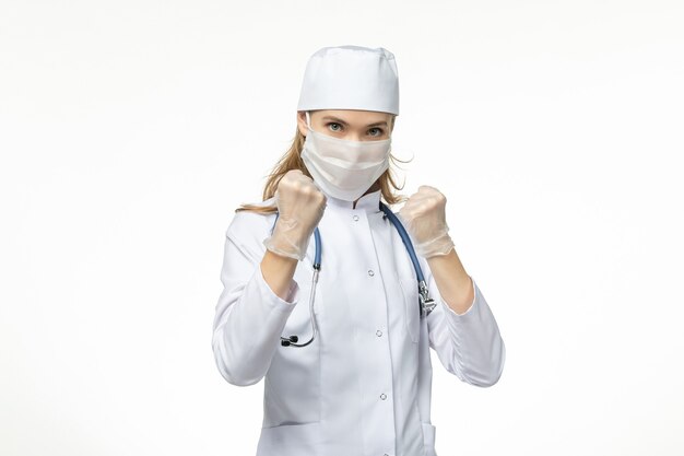 Vorderansicht Ärztin im medizinischen Anzug mit Maske und Handschuhen aufgrund von Coronavirus im Kampf gegen das hellweiße Wandkrankheitspandemie-Covid-Virus