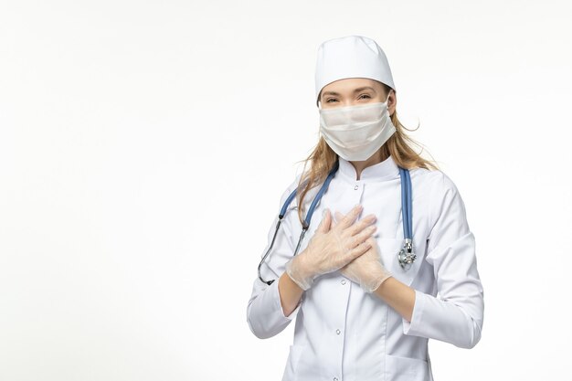Vorderansicht Ärztin im medizinischen Anzug mit steriler Maske wegen Coronavirus lächelnd auf weißer Wand Krankheit Pandemie Gesundheit covid-