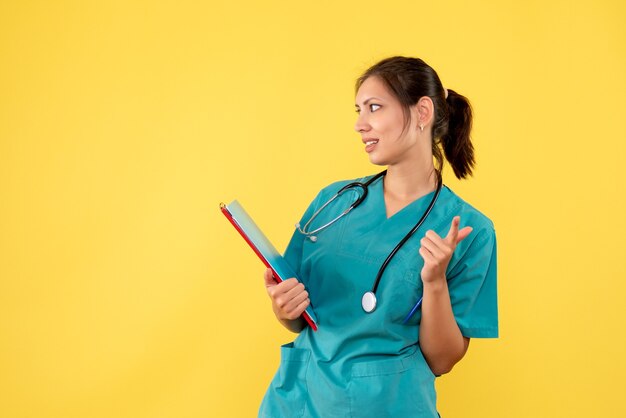 Vorderansicht Ärztin im medizinischen Hemd, das Analyse auf gelbem Hintergrund hält