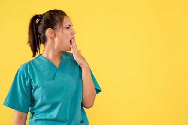 Vorderansicht Ärztin im medizinischen Hemd, das auf gelbem Hintergrund gähnt