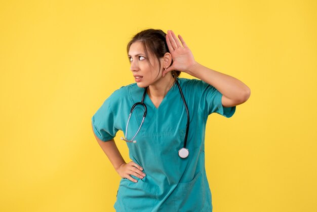 Vorderansicht-Ärztin im medizinischen Hemd, das auf gelbem Hintergrund hört