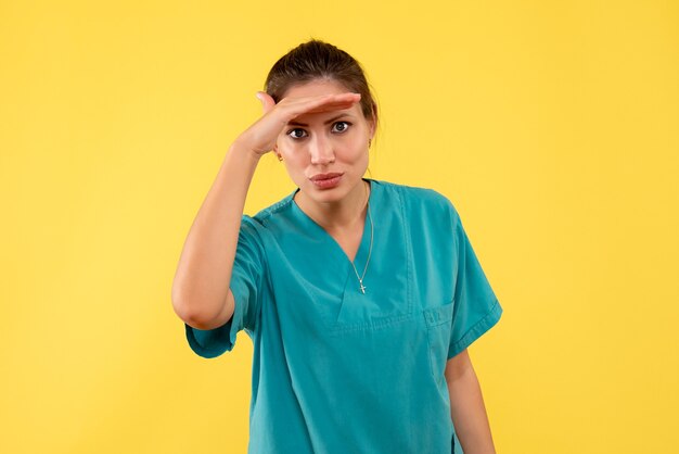 Vorderansicht Ärztin im medizinischen Hemd, das auf gelbem Hintergrund schaut