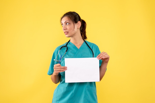 Vorderansicht-Ärztin im medizinischen Hemd, das Papieranalyse auf gelbem Hintergrund hält