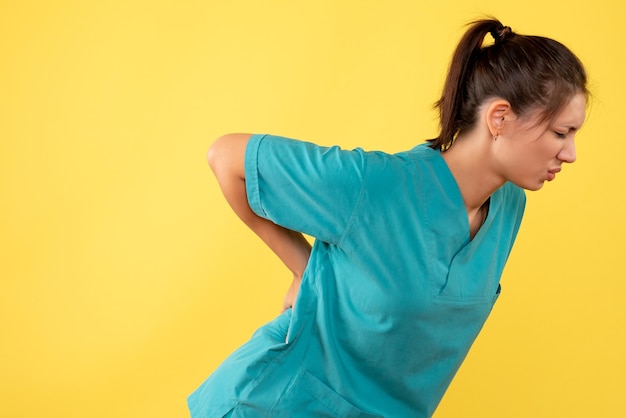 Vorderansicht-Ärztin im medizinischen Hemd, das Rückenschmerzen auf gelbem Hintergrund hat
