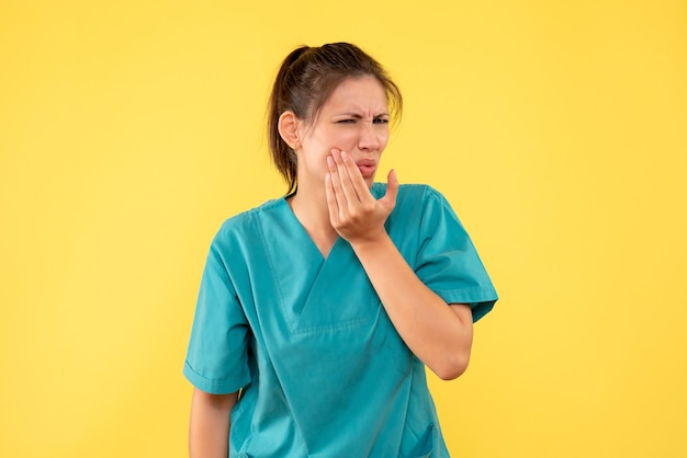 Vorderansicht Ärztin im medizinischen Hemd, das unter Zahnschmerzen auf gelbem Hintergrund leidet