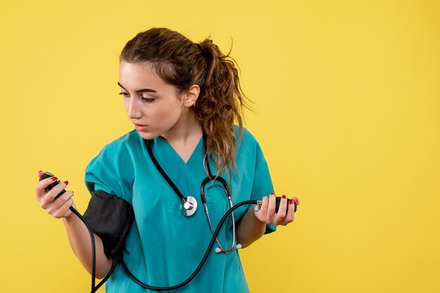 Vorderansicht Ärztin im medizinischen Hemd, die ihren Druck auf gelbe Schreibtischvirus-Gesundheitsemotions-Covid-19-Pandemieuniform prüft
