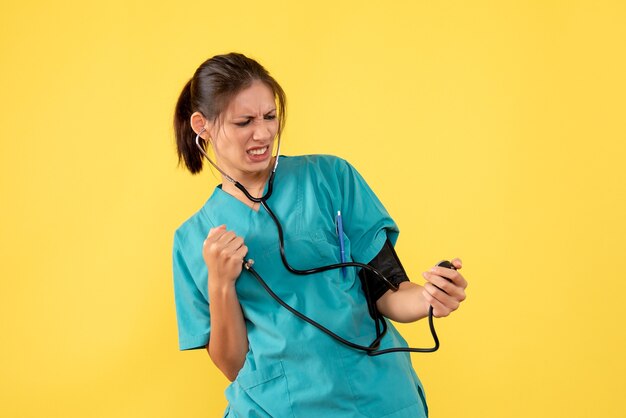 Vorderansicht-Ärztin im medizinischen Hemd, die ihren Druck auf gelbem Hintergrund prüft
