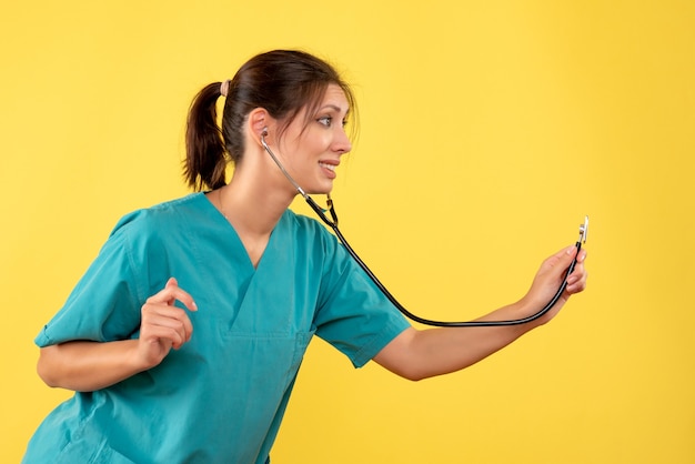 Vorderansicht Ärztin im medizinischen Hemd mit Stethoskop auf gelbem Hintergrund