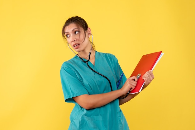 Vorderansicht Ärztin im medizinischen Hemd mit Stethoskop und Notizen auf gelbem Hintergrund